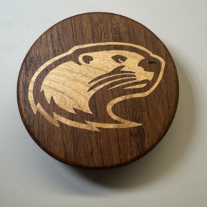 Hockey puck bottle opener with a stylized otter inlaid in maple — handmade by Langskegg