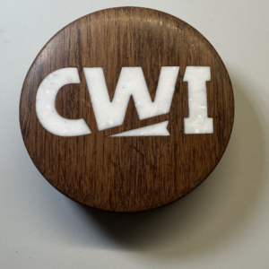 Hockey puck bottle opener with the CWI logo inlaid in white cast acrylic on a walnut body — handmade by Langskegg