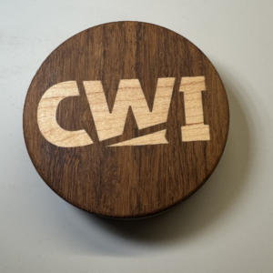 Hockey puck bottle opener with the CWI logo inlaid in maple on a walnut body — handmade by Langskegg